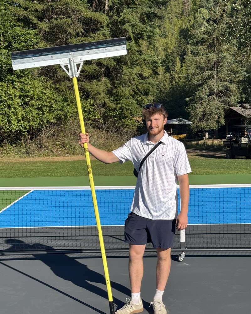 Jaden Overend holding a squeegee on a freshly painted pickleball court in the Okanagan